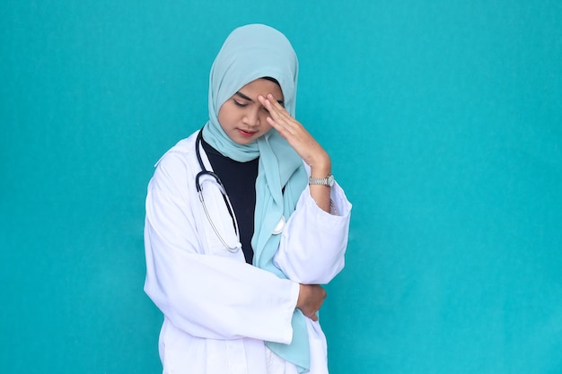 A stressed young female doctor in white coat and stethoscope isolated over green studio background