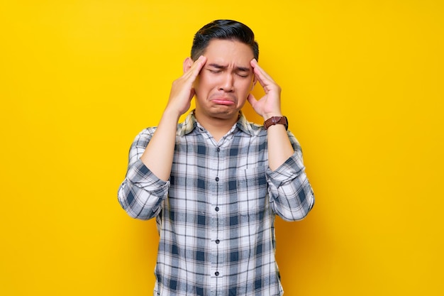 Stressed young handsome Asian man wearing casual clothes touching her temples and having headaches isolated on yellow background People lifestyle concept