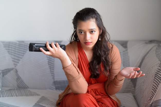 Stressed young Indian woman watching tv and looking confused in the living room at home