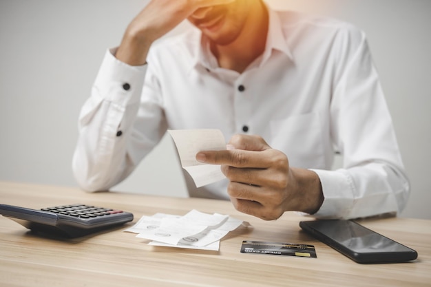 Photo stressed young male upset and worried about credit card and family budget expense cost bills and calculator on desk in home, plan money cost saving, investment, business finance and expenses concept