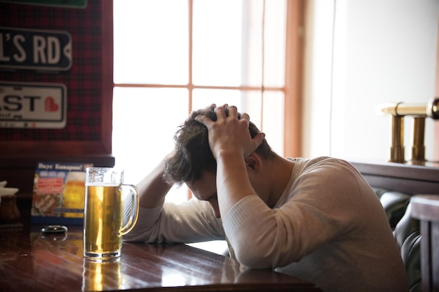 사진 스트레스를 받는 젊은이는 술집에서 맥주를 마신다 남자는 머리를 안고 있다