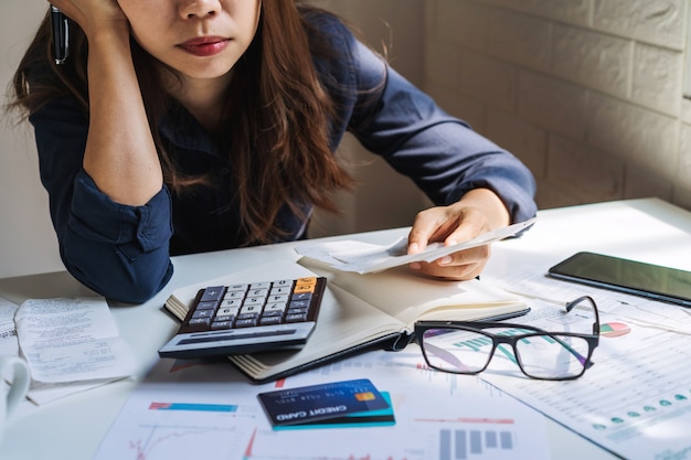 Stressed young woman checking bills, taxes, bank account balance and calculating expenses in the living room at home