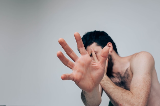 Stressful confused guy show hand and try to hide form camera. Alone in room in confused mode or mood. Suffer from depression and mental sickness.