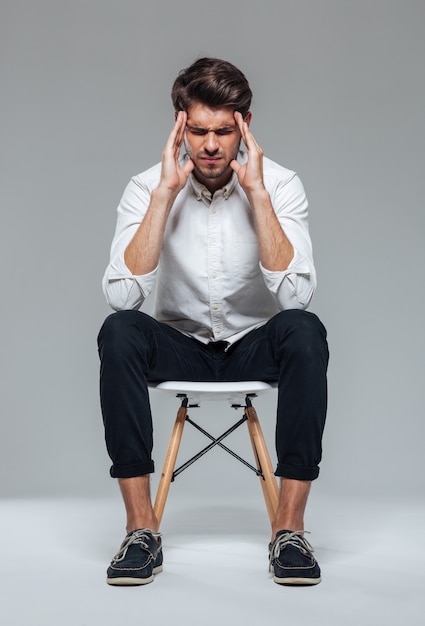 Stressful depressed man touching his temples and having headache over gray wall