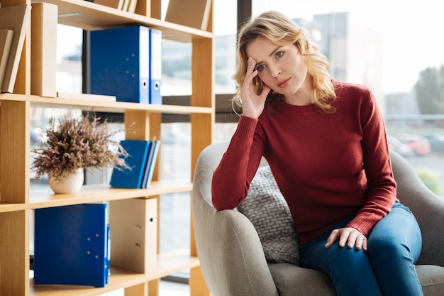 Situazione stressante. triste bella giovane donna che guarda davanti a lei e si tiene la fronte mentre si trova in una situazione stressante