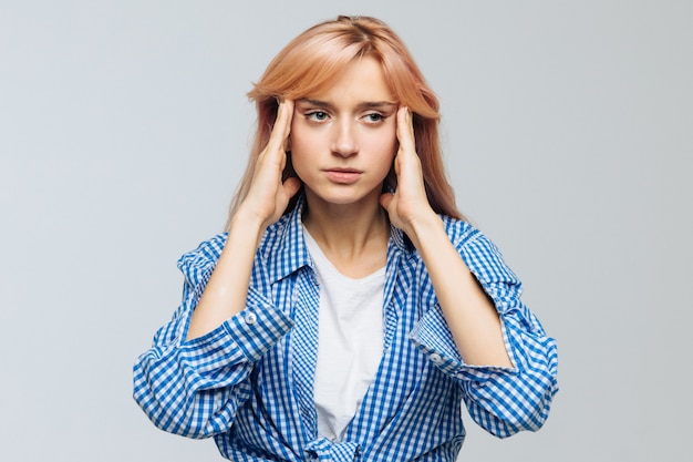 Stressful teen woman has a headache, tries to concentrate, gather with thoughts, keeps hands on temples