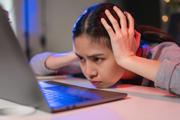 Stressvolle Aziatische zakenvrouw die op de stoel zit en 's nachts op het laptopscherm op kantoor kijkt.