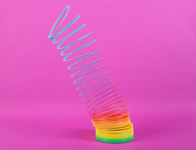 Растянутая радужная пластиковая разноцветная спиральная обтягивающая игрушка на розовом фоне Минимализм