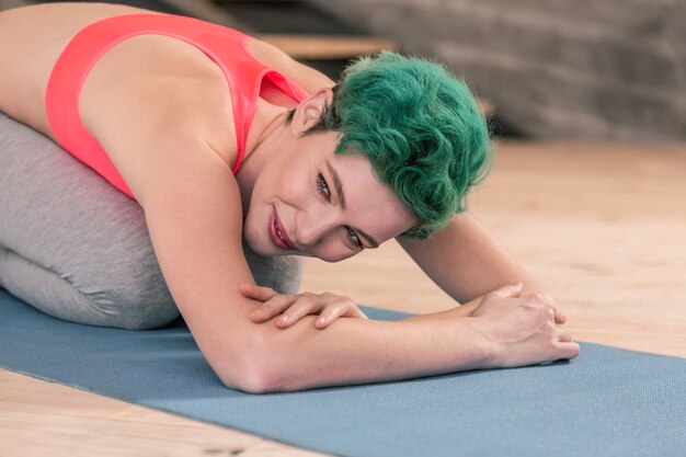 Stretching after fitness. Appealing young green-haired woman wearing sport clothes stretching after fitness