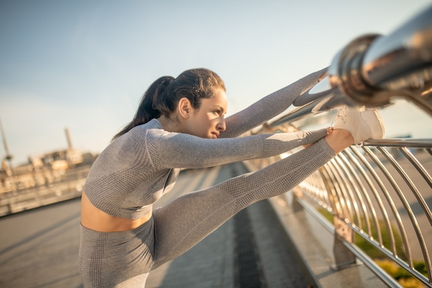 Stretching legs. Dark-haired girl in grey sportswear training her flexibility