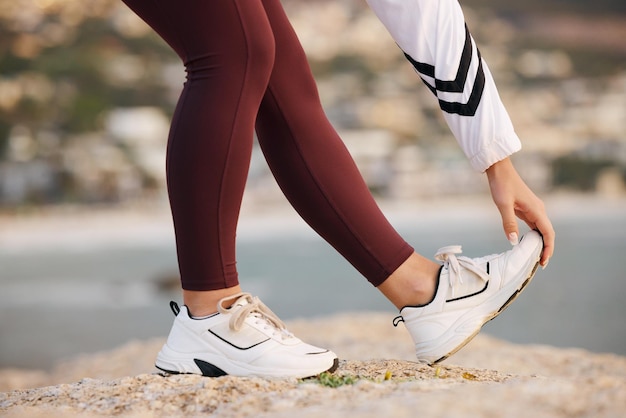 Stretching legs and woman on a beach rock start fitness and yoga exercise in nature of Portugal Warm up training and feet of an athlete at the ocean for spiritual health cardio or pilates