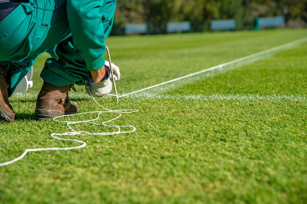 草の上に白いペンキを使ってサッカー場を裏打ちするためのロープを伸ばす