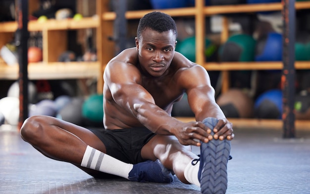 Stretching training and portrait of black man in gym for sports workout and performance Wellness exercise and fitness with athlete and warm up legs on floor for cardio endurance and energy