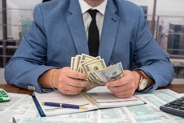 Strict angry businessman in a suit from a stylist makes calculations on his own business at the table in the office The concept of tax forms and business