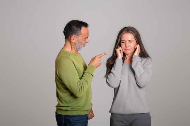 Strict angry caucasian aged husband scolds his wife lady covers ears