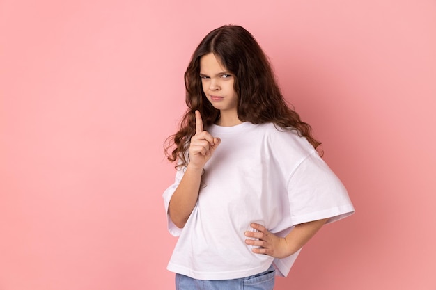 Tshirt를 입고 심각하게 손가락을 가리키고 카메라 경고를 보고 있는 엄격한 강력하고 어린 소녀