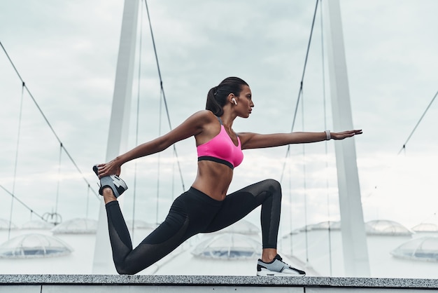 Striking the pose. Modern young woman in sports clothing stretching while warming up outdoors