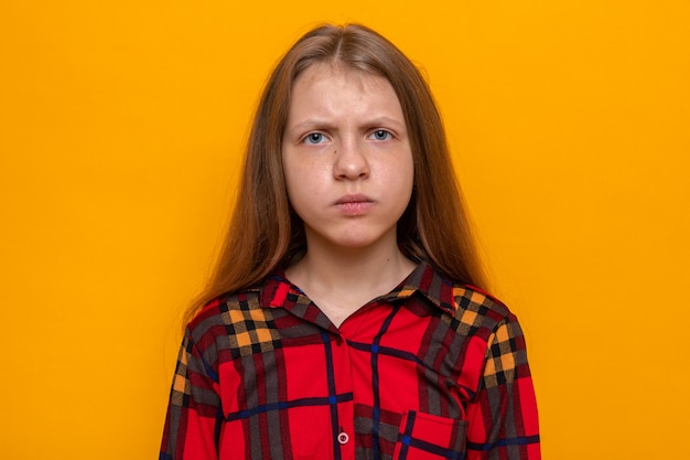 Strikt mooi meisje dat rood overhemd draagt dat op oranje muur wordt geïsoleerd