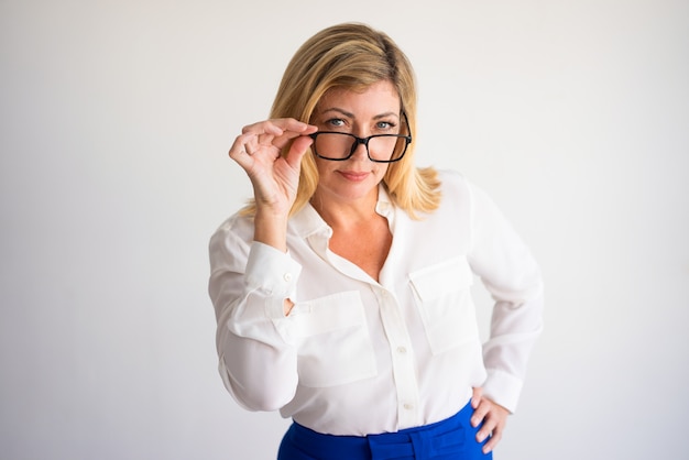 strikte aantrekkelijke blonde vrouw op middelbare leeftijd die camera over haar glazen bekijken