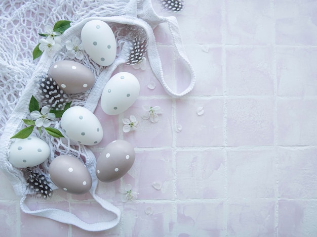 String bag with Easter eggs and spring blossom on pink tile background