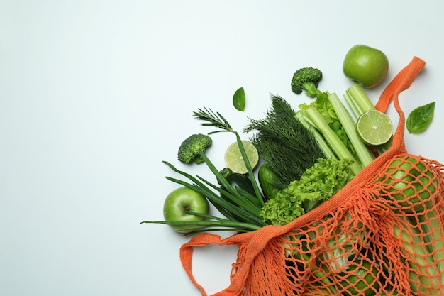 Photo string bag with green vegetables on white