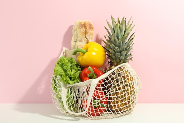 String bag with grocery on white table against pink background