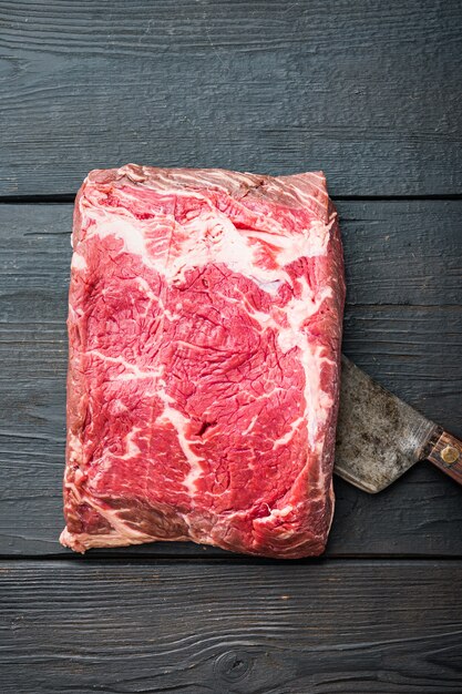 Strip loin steak, raw marbled beef meat, on black wooden table, top view