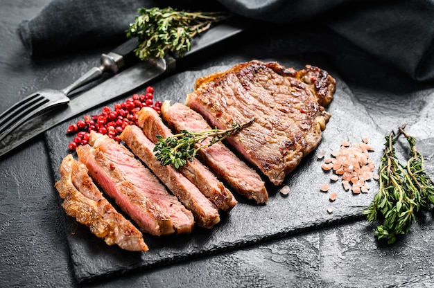 strip new York steak on a stone plate on Black table.