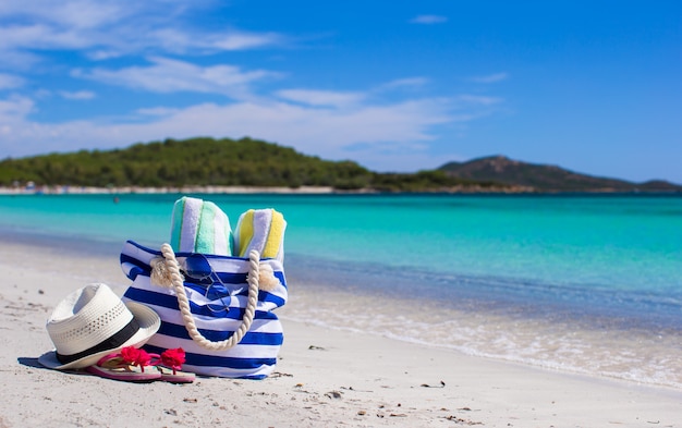 Borsa a strisce, cappello di paglia, crema solare e frisbee sulla spiaggia tropicale di sabbia bianca