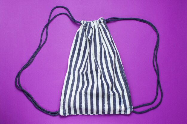 Photo striped beach backpack on purple table. top view