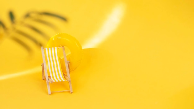 Foto sedia da spiaggia a righe e anello da nuoto su sfondo giallo con palma sfocata in primo piano