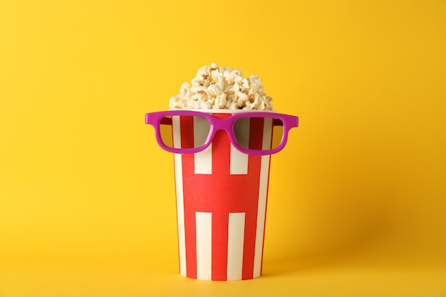 Photo striped bucket with popcorn and glasses on yellow background