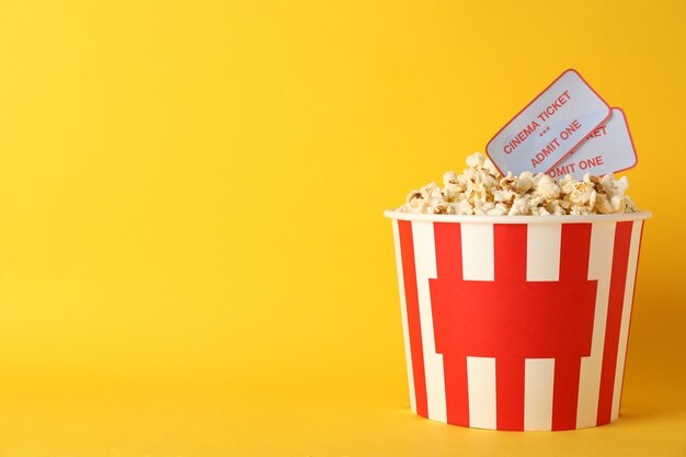 Striped bucket with popcorn and tickets on yellow background