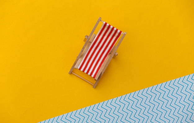 Foto mini sdraio da spiaggia a righe su giallo blu. simbolo delle vacanze al mare, resort