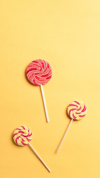 Striped spiral multicolored lollipops on a yellow background. sweet dessert. school snack. vertical image. copy space