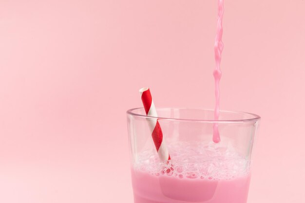 Striped straw in a glass of strawberry milkshake isolated on pink