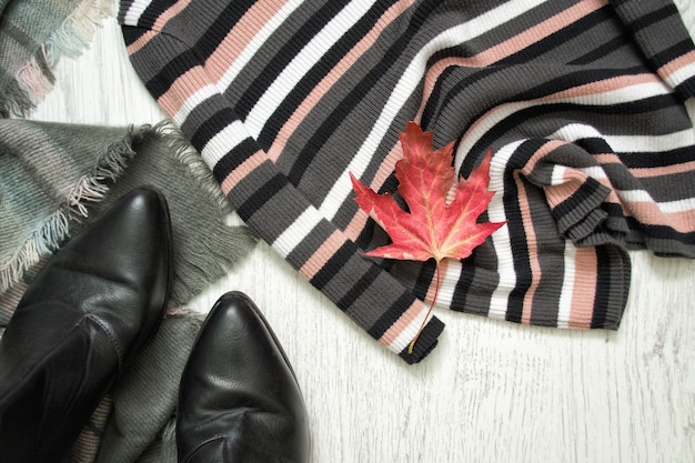 ストライプのセーター、黒いブーツ、赤いカエデの葉。ファッショナブルなコンセプト
