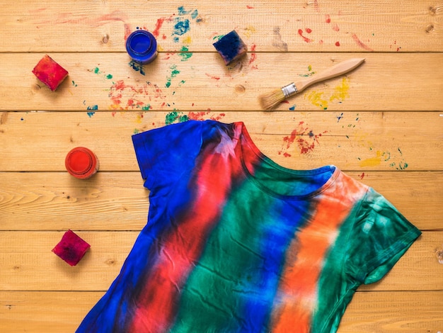 A striped tie dye tshirt with paint on a wooden background Flat lay