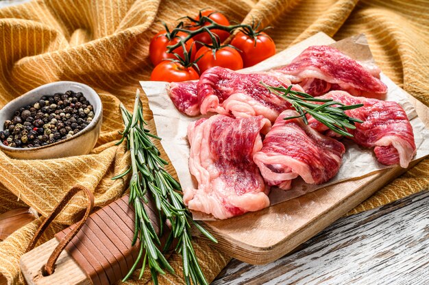 Strips of marbled beef, quick steak on cutting board. White wooden background. Top view