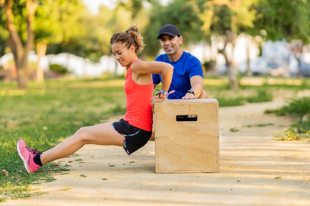 Photo strong adult woman wearing sports clothes using jumping box in the park and working out.