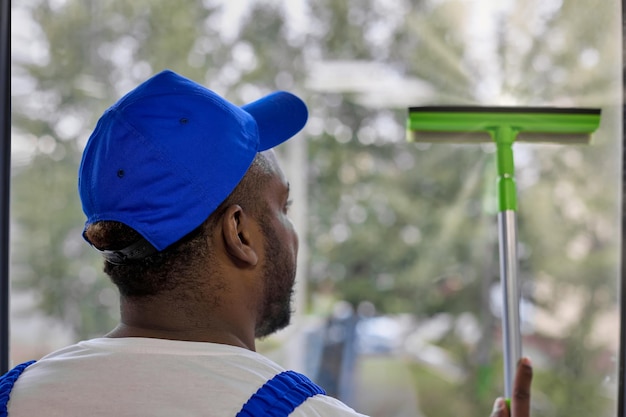 Strong AfricanAmerican man in white Tshirt and cap with window cleaning brush