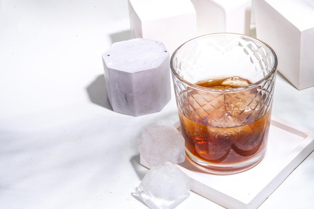사진 강한 알코올 음료 유리 여름 햇빛 복사 공간이 있는 흰색 타일 배경에 얼음 조각이 있는 코냑 또는 위스키 한 잔