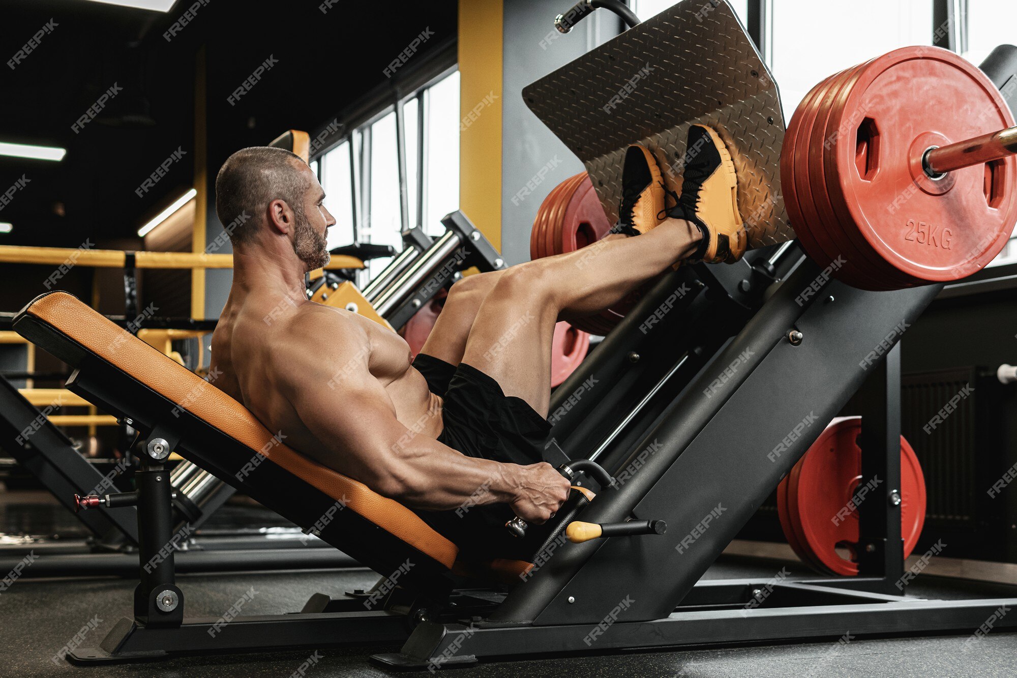 체육관에서 앉아 레그 프레스 운동을 하는 강하고 근육질의 보디빌더 | 프리미엄 사진