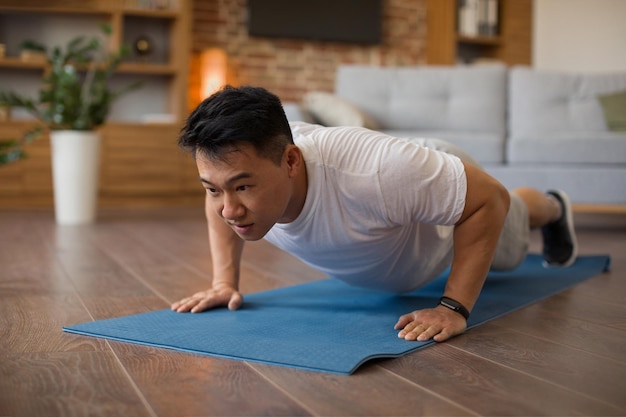 Сильный азиатский зрелый мужчина делает силовые тренировки, отжимается на спортивном коврике, имея домашнюю тренировку