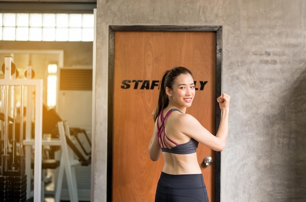 Photo strong asian woman posture standing and lifting up arms and exercises muscle at gym