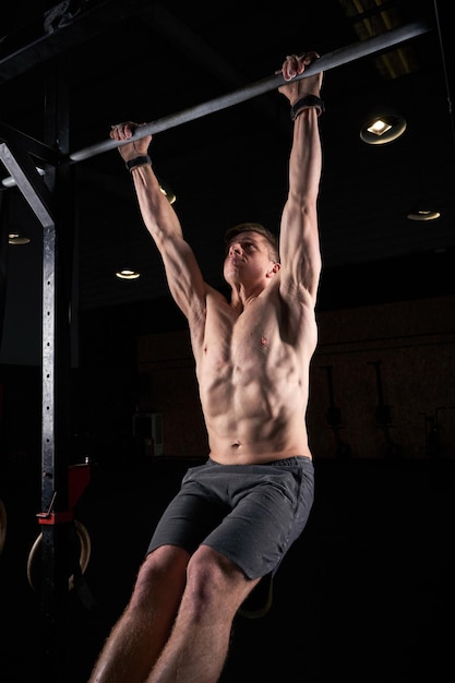 Strong athlete performing pull ups on bar in darkness