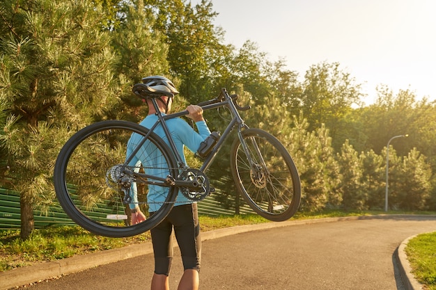 Strong athletic male cyclist in sportswear and protective helmet carrying his bike after training in