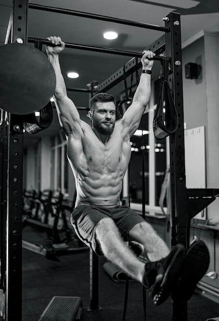 Strong athletic man fitness model. Guy with nacked torso showing six pack abs while pulling up. Black and white photo.