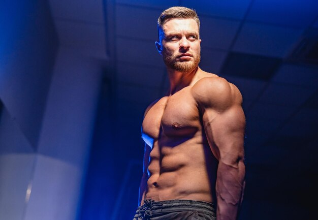 Strong athletic man fitness model torso showing six pack abs isolated on dark background with blue filter Closeup