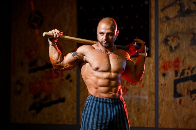 Strong athletic man posing with a sports hammer on the background of the gym. A strong bodybuilder with perfect abs, shoulders, biceps, triceps and chest.